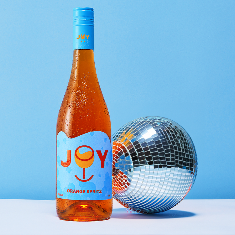 A bottle of Joy Orange Spritz with a blue backdrop and a discoball.