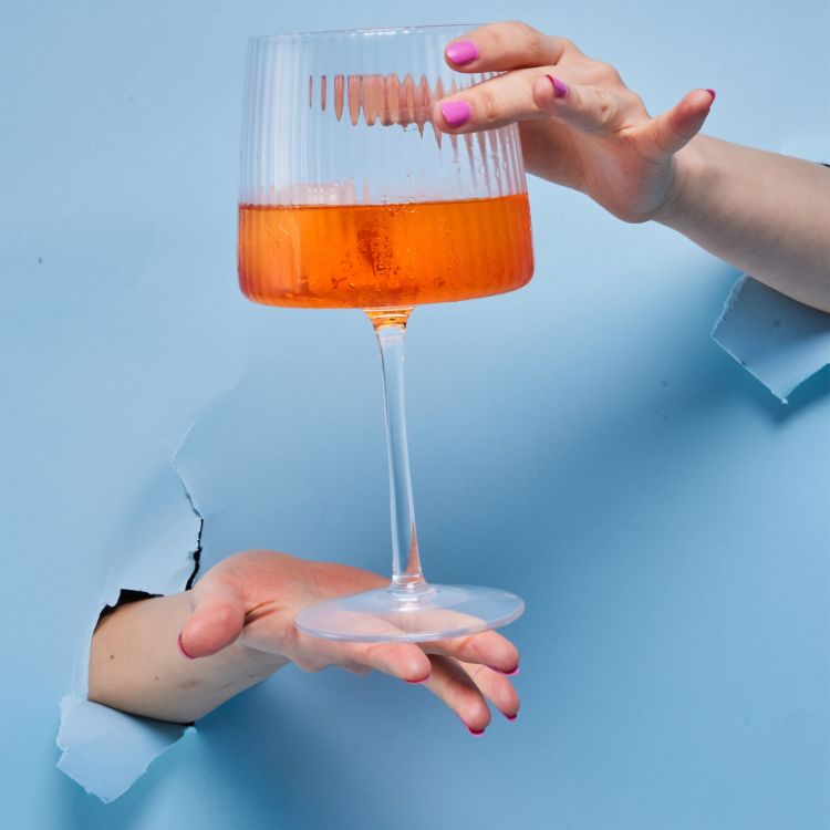 A glass of JOY Orange Spritz wine being held in front of broken blue paper.